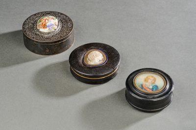 trois petites boîtes noires ornées de photos de personnes, posées sur une table