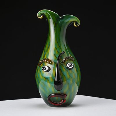 un vase vert orné d'un visage, posé sur une table