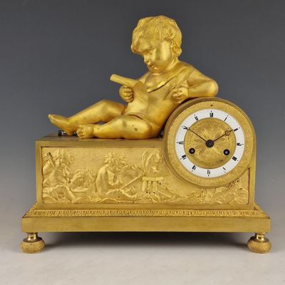 figurine en or représentant un garçon assis sur une horloge, en train de lire un livre