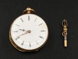 une montre de poche en or et une clé posées sur une surface noire