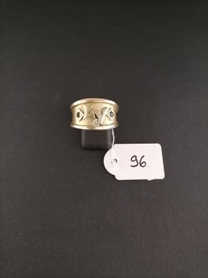 a gold ring with a black band and a white tag on a black surface