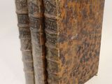 trois vieux livres sont empilés sur une surface blanche
