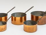 six casseroles et cuillères en cuivre sont alignées sur une surface blanche