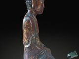 statue of a person sitting on the ground next to a bottle of wine