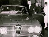 black and white photo of a group of people standing around a car