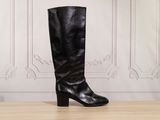 black leather boots on a wooden table in front of a white wall