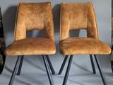 pair of brown leather chairs with black metal legs against a gray wall