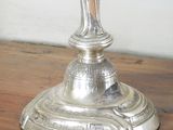 a silver vase on a wooden table with a white wall in the background