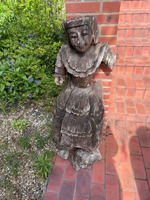a wooden statue of a woman standing on a brick walkway