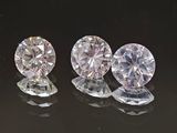 trois diamants ronds taille brillant sur une surface réfléchissante