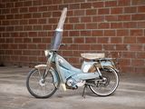 a small blue moped parked in front of a brick wall