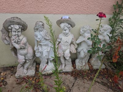 quatre statues d'enfants coiffés de chapeaux et tenant des fleurs, devant un mur