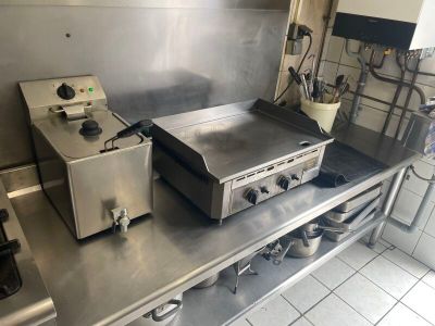 plan de travail en acier inoxydable dans une cuisine professionnelle équipée de deux friteuses et d'une cuisinière