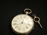 a silver pocket watch and a key on a black surface