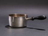 a silver sauce pot with a black handle on a table