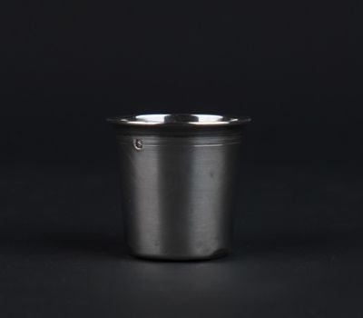 an empty metal cup on a black surface with a black background