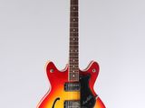 une guitare électrique rouge et jaune posée sur une surface blanche