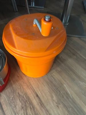 un récipient orange posé à côté d'un saladier en métal, par terre