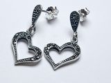 une paire de boucles d'oreilles en forme de cœur, ornées de diamants noirs et blancs, sur fond blanc