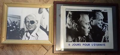 Deux photos encadrées représentant des hommes sont posées sur un plancher en bois, à côté d'un portrait d'un homme