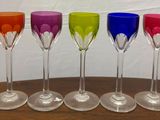 six verres à vin colorés alignés sur une table en bois