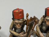 three figurines of monkeys playing musical instruments on a white surface