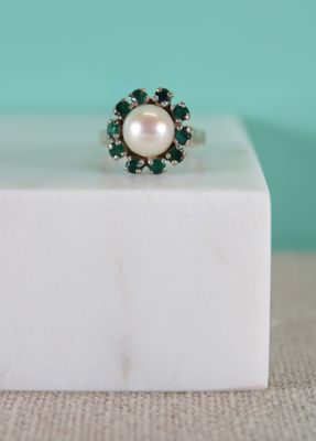 a close up of a pearl and emerald ring on a white marble block