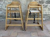 two wooden high chairs sitting next to a stone wall