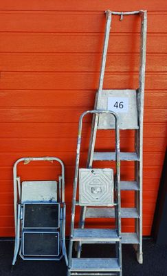 three ladders and a chair in front of an orange wall
