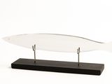 un poisson en verre posé sur un socle en bois, sur fond blanc