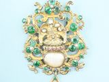 a close up of a gold pendant with green and white stones