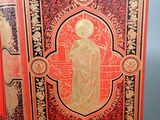 an old book with gold and red cover sitting on top of a table