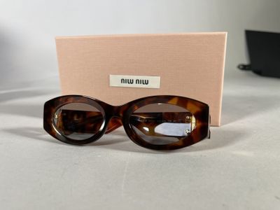 brown sunglasses on a table next to a pink box and a laptop