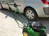 une tondeuse à gazon verte posée par terre à côté d'une voiture argentée