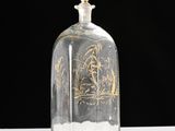 a clear glass bottle with a gold design on it
