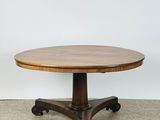 une table ronde en bois munie de roulettes, posée sur un sol recouvert de moquette