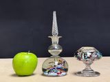 a green apple sitting next to a glass vase and a glass candle holder