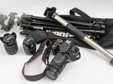 un appareil photo, un trépied, un sac pour appareil photo et d'autres objets disposés sur une surface blanche