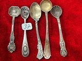 cinq cuillères en argent et une cuillère portant une étiquette avec un nom, posées sur un tissu rouge