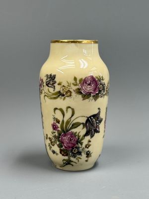 un vase jaune orné de fleurs violettes, posé sur un fond gris
