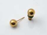 une paire de boucles d'oreilles à tige en forme de boule dorée posées sur une surface blanche