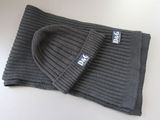 un bonnet et une écharpe en tricot gris posés sur une surface blanche