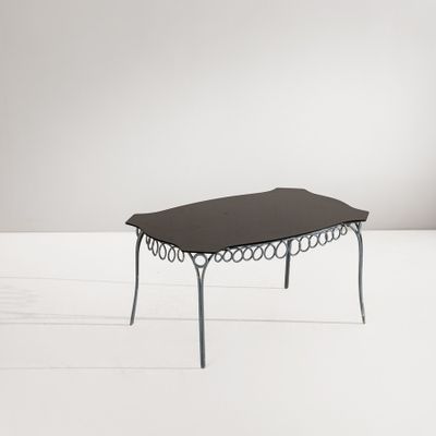La table est en métal et possède un plateau en verre noir.