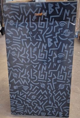 un réfrigérateur noir recouvert de graffitis, dans un entrepôt