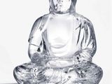 une statue en verre représentant un Bouddha assis sur une surface blanche