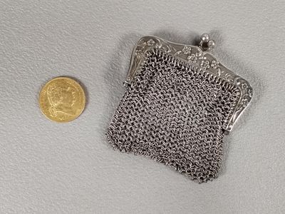 une petite bourse en argent posée à côté d'une pièce de monnaie sur une surface blanche