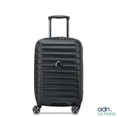 La valise noire repose sur ses roulettes, posée sur une surface blanche.