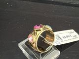 une bague en or ornée d'une fleur rose, posée sur un socle en verre