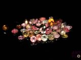 un gros plan sur un tas de diamants de différentes couleurs posés sur une surface noire