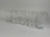 six clear glasses lined up in a row on a white surface